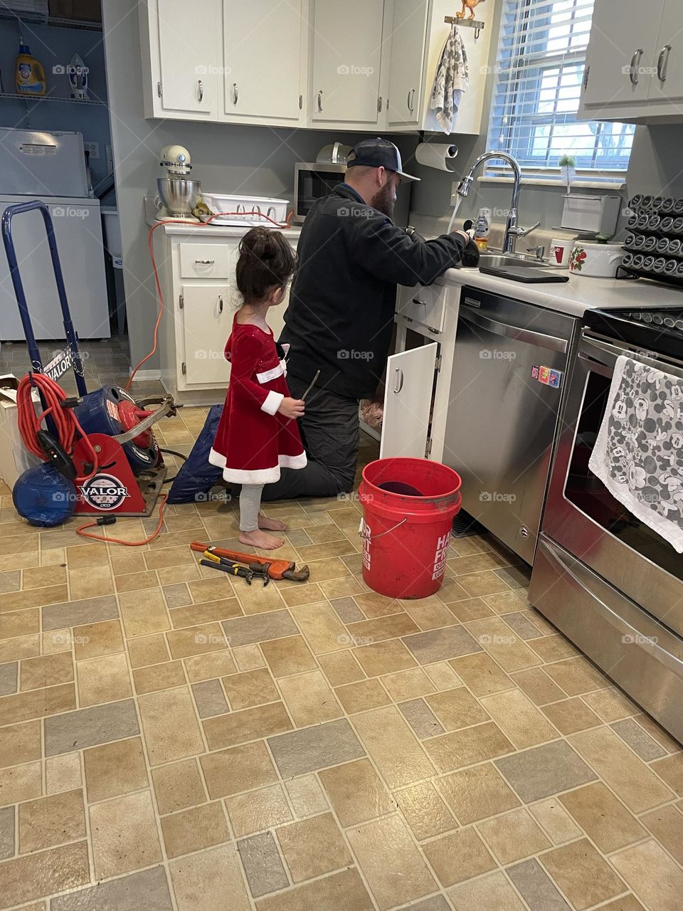 Little watches as plumber fixes sink, toddler girl watches plumber work, plumber fixing sink, plumber fixes kitchen sink, toddler helping plumber 