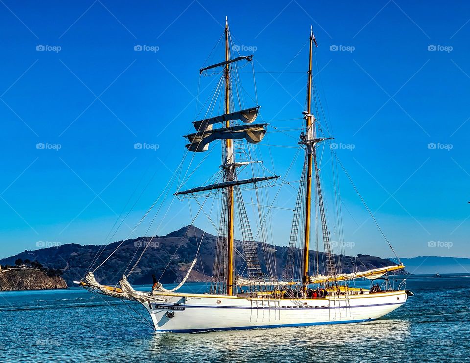 Beautiful vintage antique sailboat sailing on the San Francisco Bay in California viewed from Sausalito with mountains in the background and a clear blue sky 