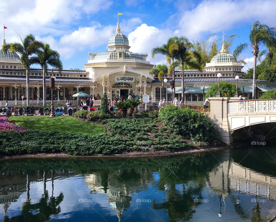 Looking across the lagoon at the Crystal Palace in the Magic Kingdom. A beautiful day, bright blue sky with white wispy clouds and a warm sun.
