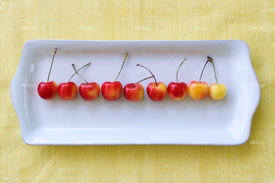 Fruits! - Rainier cherries arranged horizontally by color gradation on a white rectangular plate on a yellow surface in natural light
