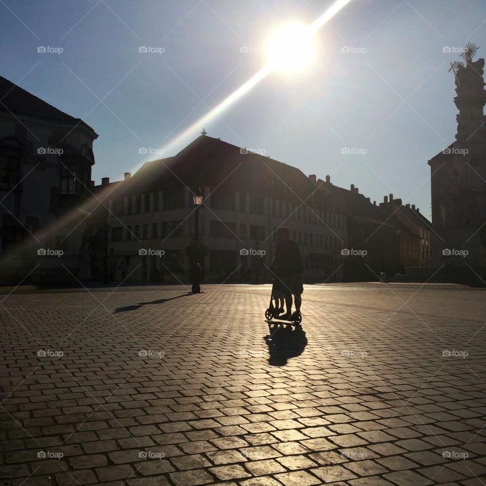 Budapest … a father and child share a scooter ride together across a square 