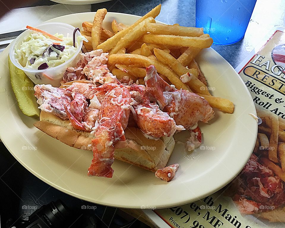 A huge New England Lobster Roll with the lobster meat overflowing, French fries and coke slaw