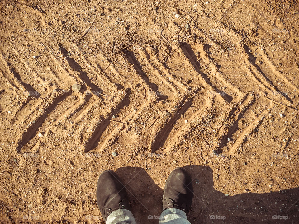 Mans Feet On The Soil Ground In Front Of Tractor Footprints
