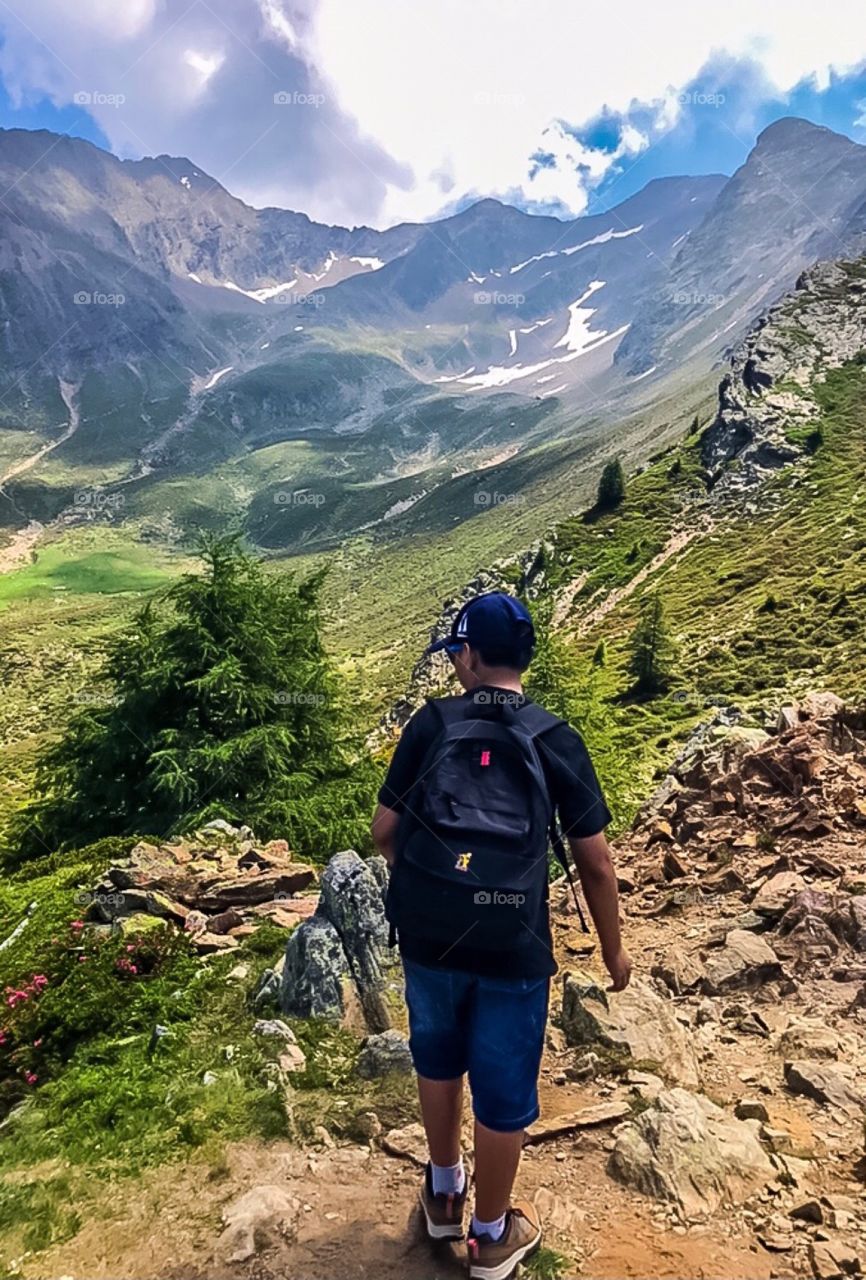 A boy wearing a black backpack is hiking in the mountain