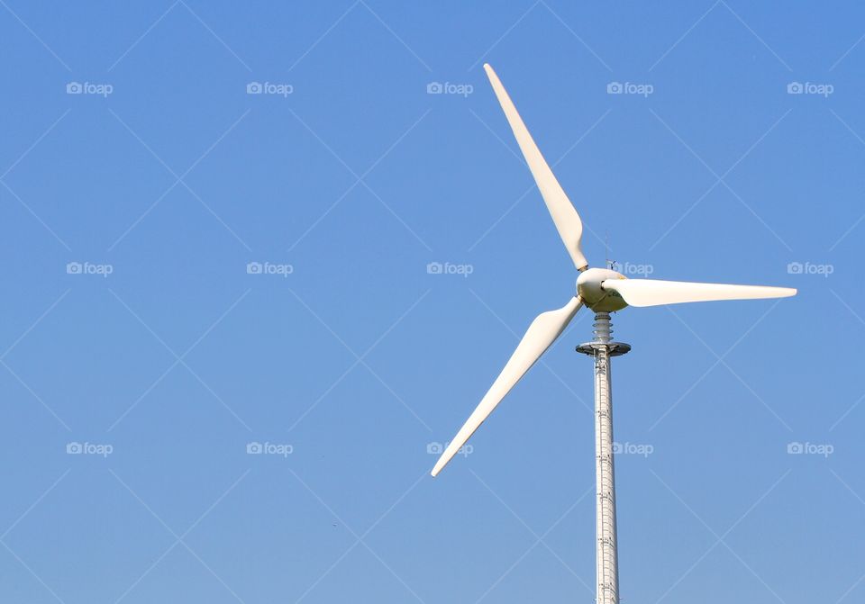 A wind turbine generating clean electricity through wind power with a bright blue sky behind.