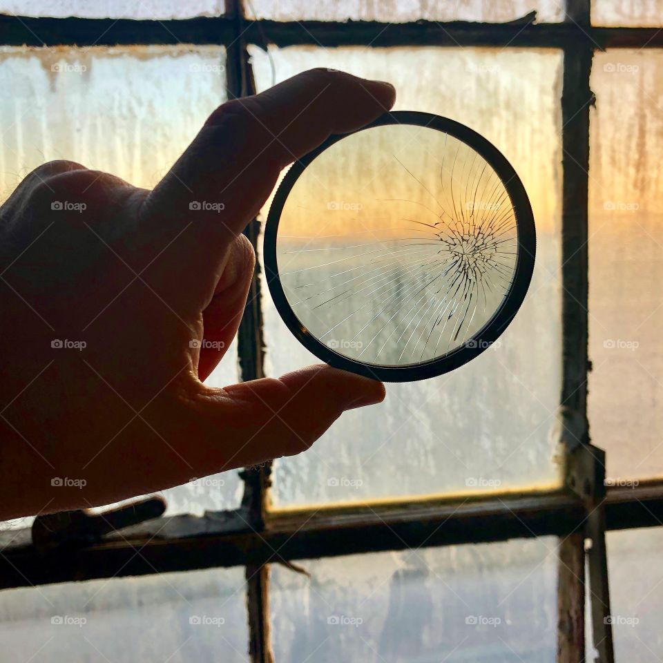 Cracked lens filter held up to a dirty factory window. 