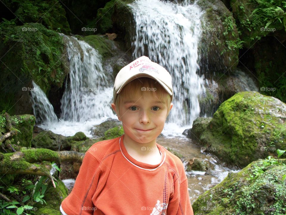 Little boy standing in front of waterfall