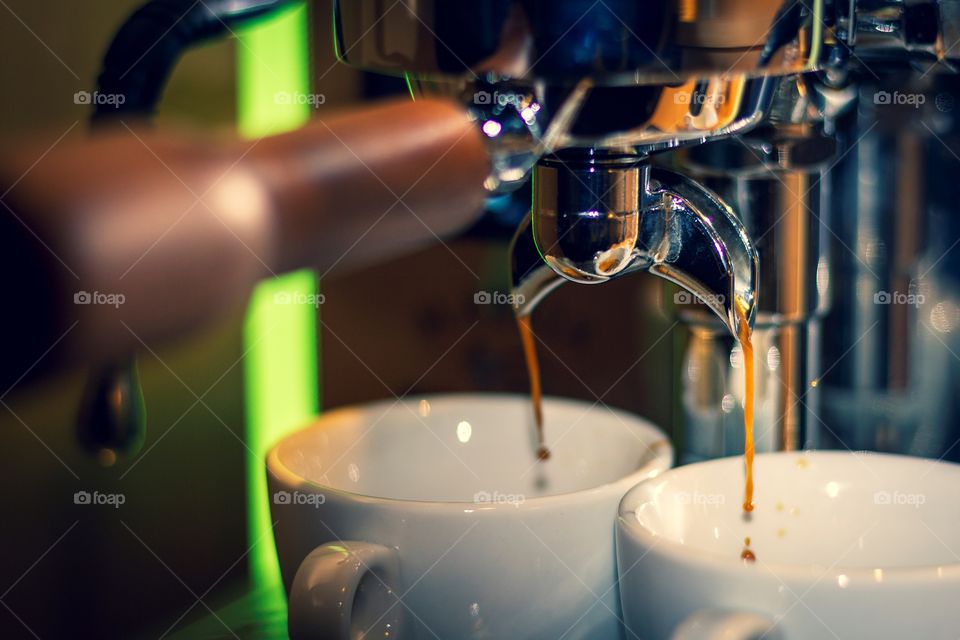 A portrait of a coffee machine making two cups of coffee. the coffee is pouring out into the two cups.