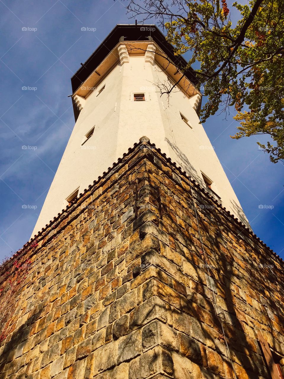 The tower is painted in cream color, the four sides below are covered with brown stones, when standing on the tower you can see a wonderful panorama around. I standing look up at the blue sky and yellow leaves