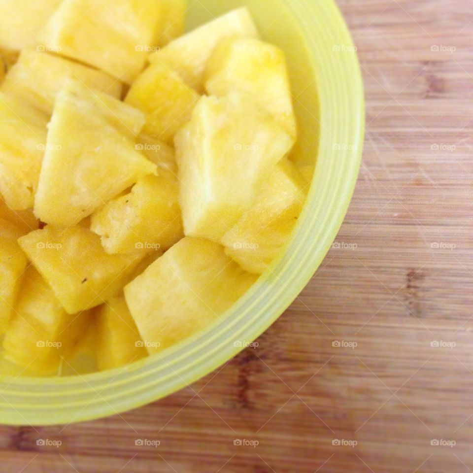 Sunny Pineapple. Freshly cut pineapple in a yellow bowl on a wooden cutting board.