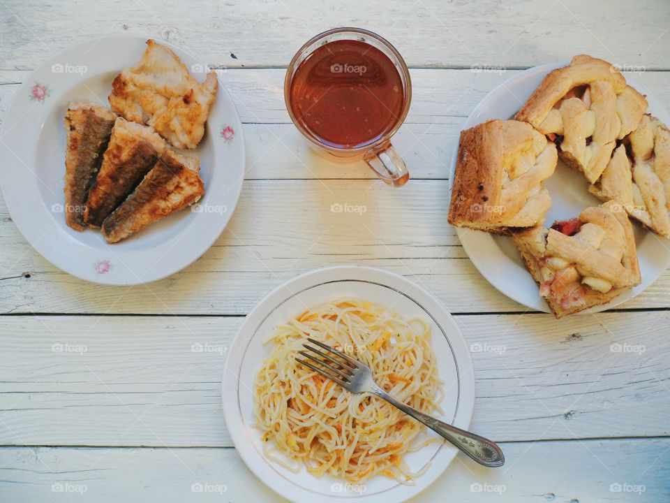 noodles in a dish, homemade cake, fried fish and a cup of tea on the table