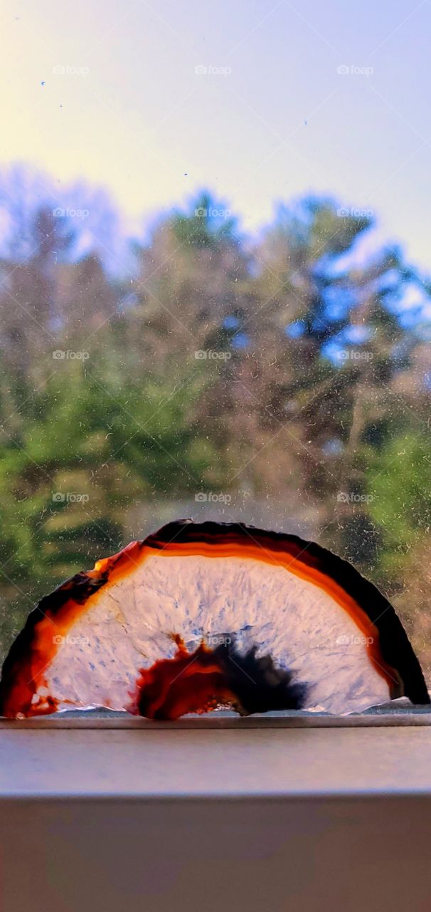 Geode looks like a sunrise or sunset as it sits against the woods as a backdrop. Colorful Geode.
