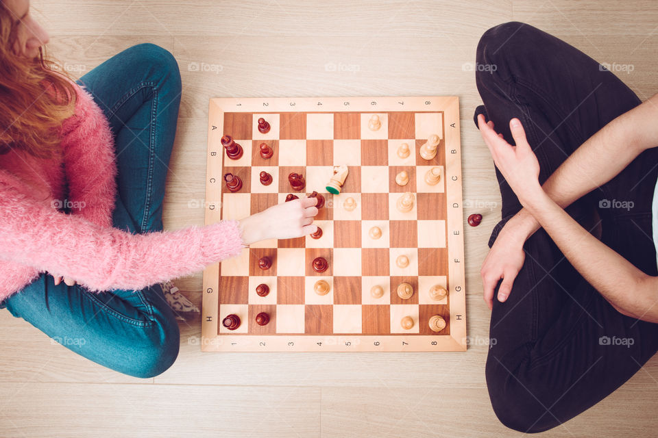 Girl and boy playing chess at home. Girl moving her piece and capturing her opponent's knight. Teenagers sitting on a floor. View from above. Copy space for text at the top and bottom of image