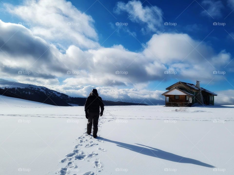 man with his back to the snow heads towards a mountain hut