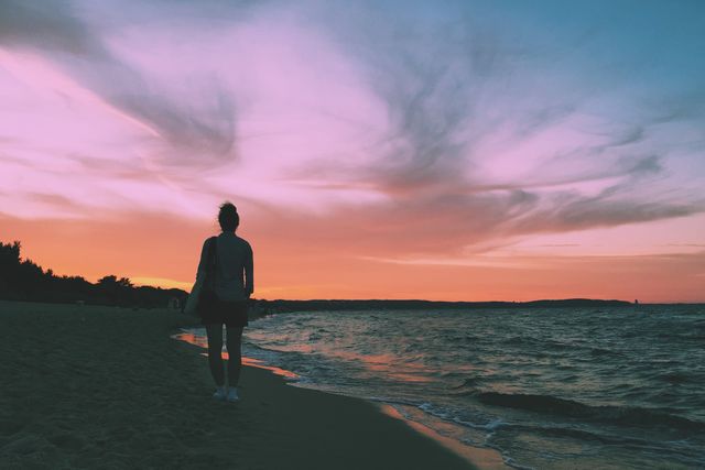 A woman walking alone on the beach at sunset