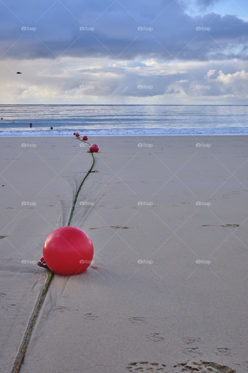 
"Red balls and a line marking a designated area on the sandy beach, captured before sunrise."