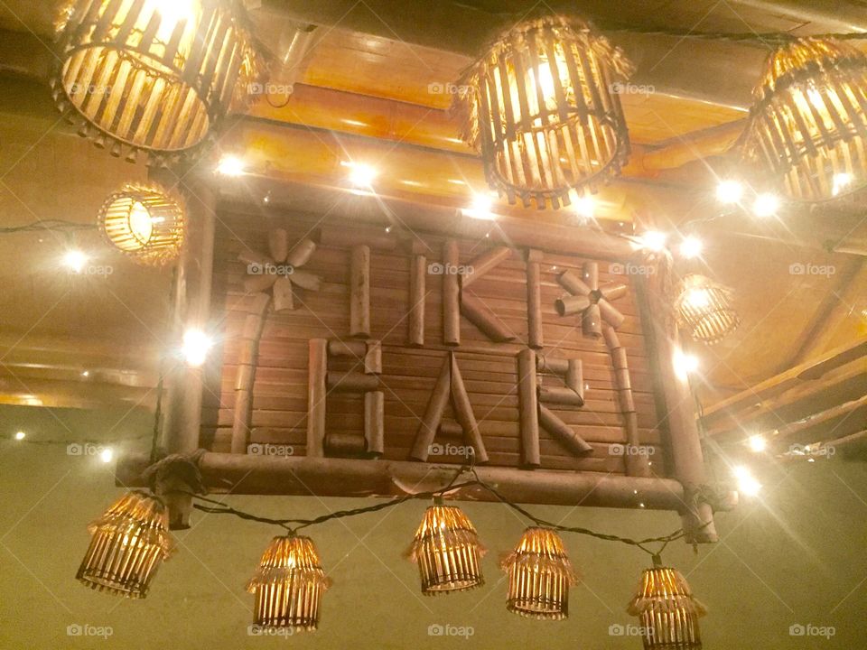 A bamboo tiki bar sign surrounded by a string of lantern lights