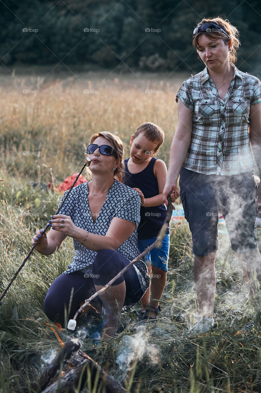 Women roasting a marshmallows over a campfire on meadow. Vacations close to nature. Candid people, real moments, authentic situations