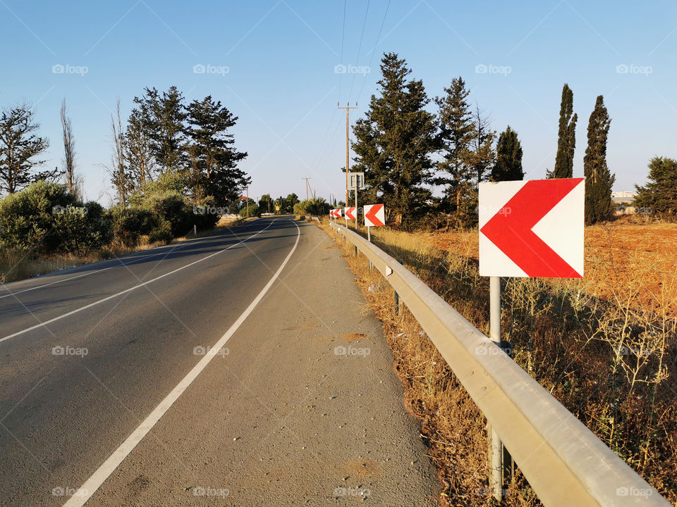 Warning sign post on the curve bend beside the right side of the main road. Selective focus on the warning sign post. Copy space is on the left side.