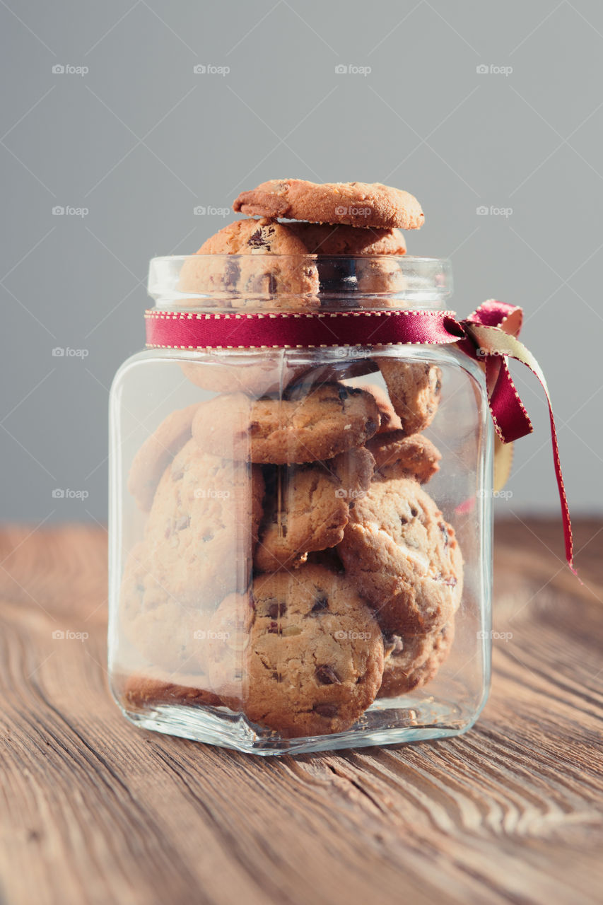 Big jar filled with oat cookies standing on a wooden table. Plain background. Portrait orientation