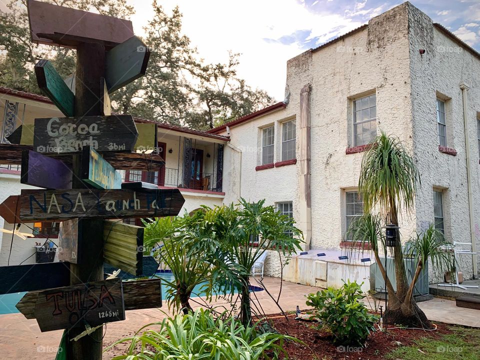 White and red spanish old style architecture residential large house built in the early 1900s. Many windows on the side of the house with aging signs with charming pretty style and beautiful landscaping with pool, chairs, focus on destinations arrows