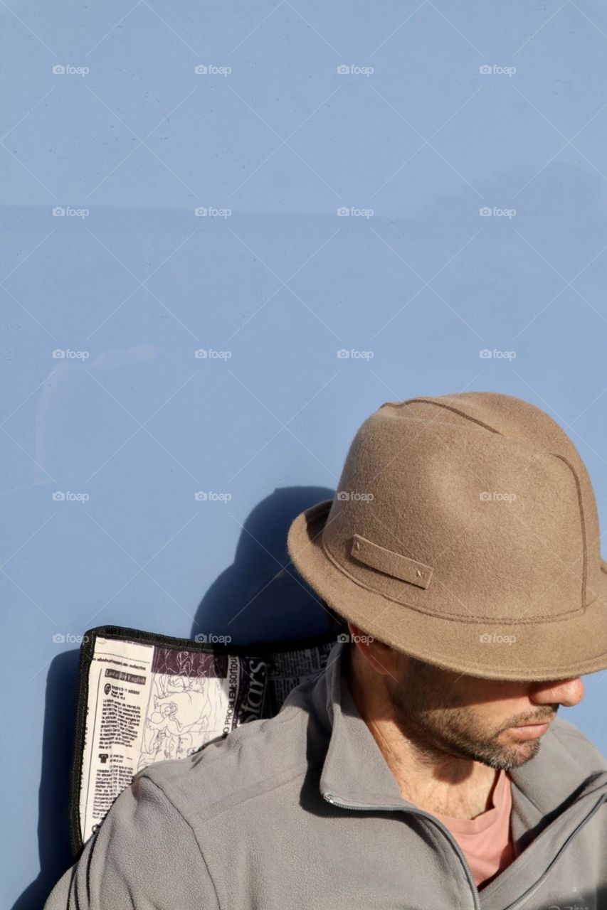 A man with hat sit in the sun on blue background 