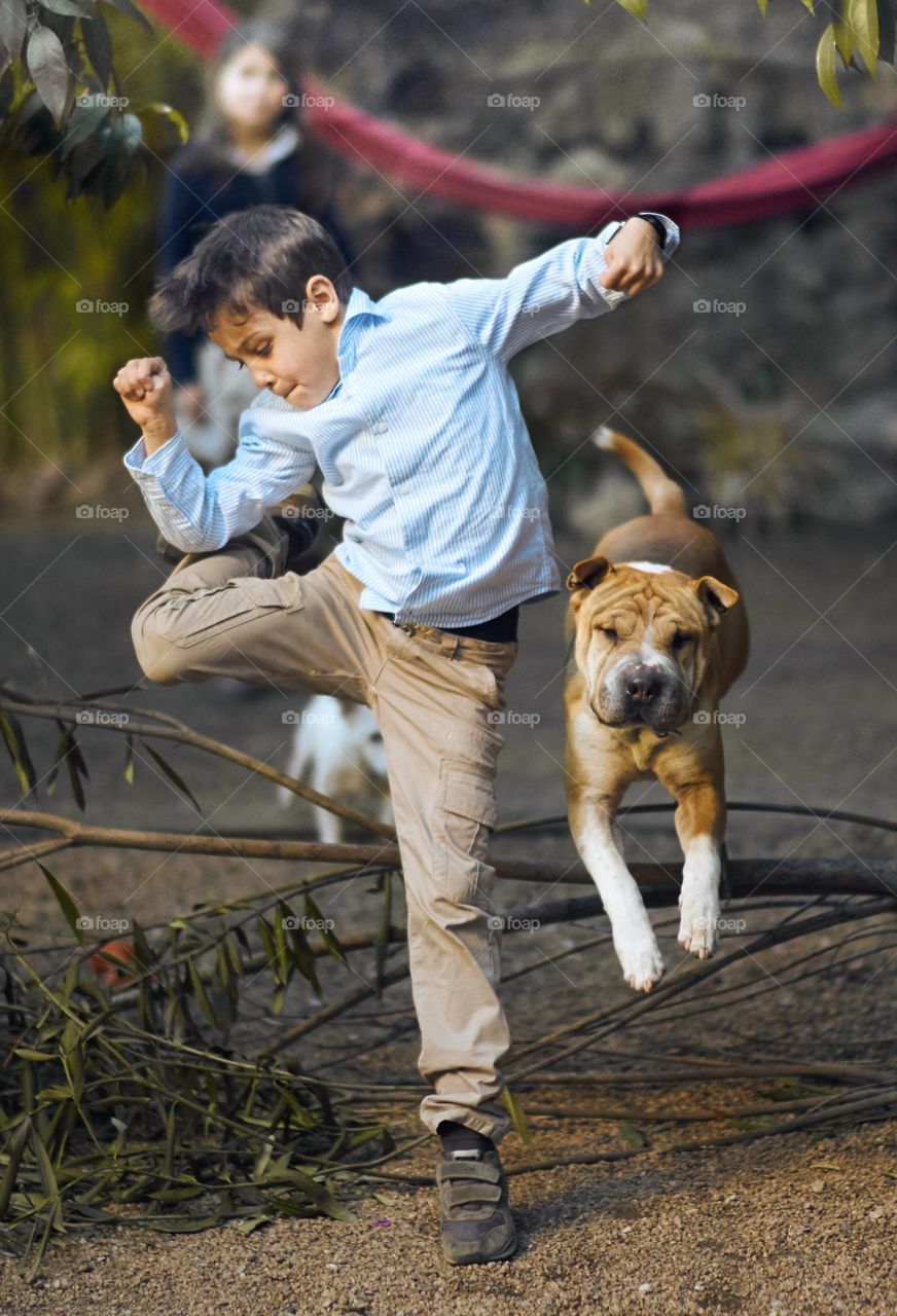 A boy and dog jumping over fallen tree branch on street