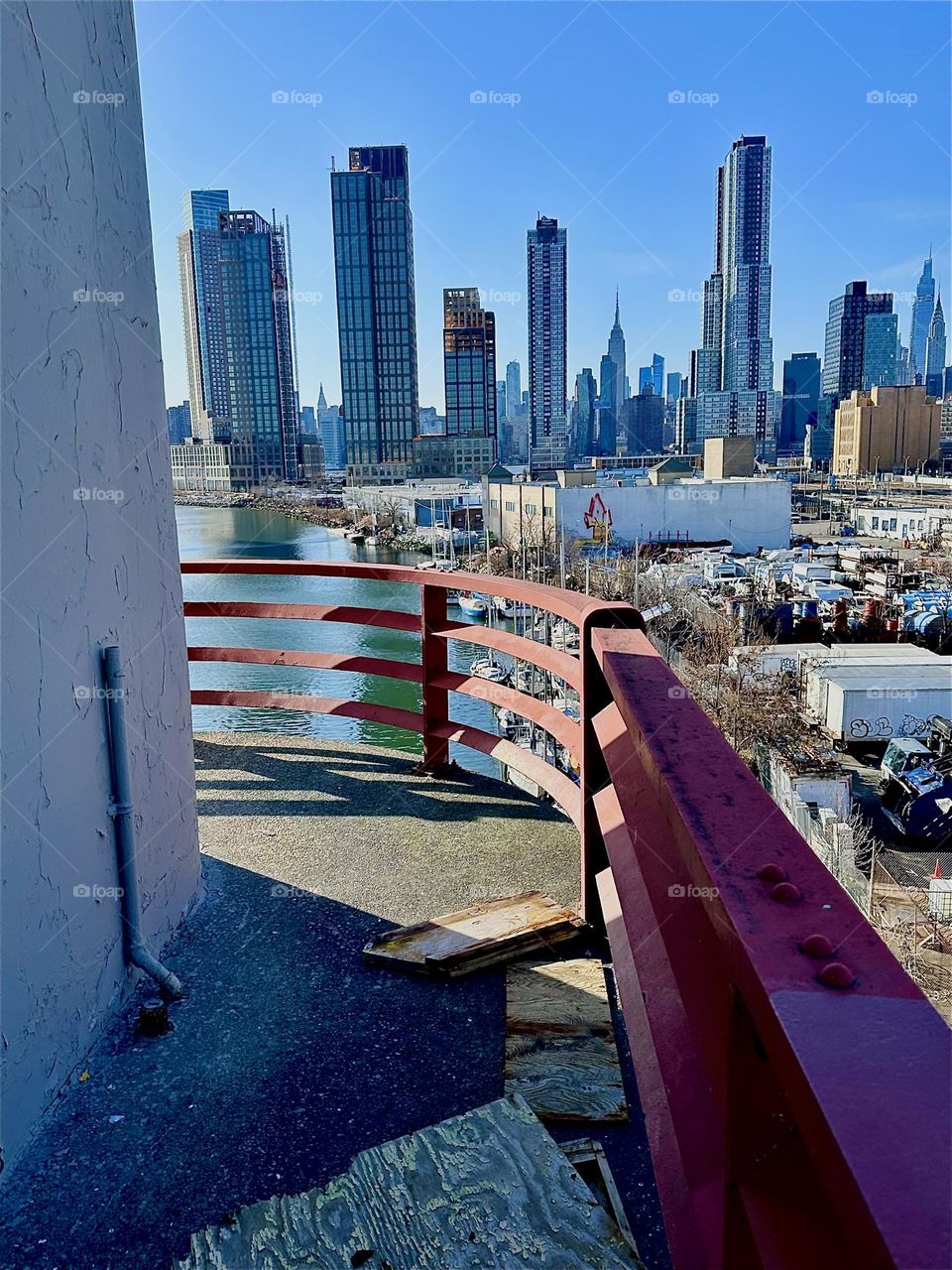 This is “Newtown Creek” seen from the central outpost of the “Pulaski Bridge” that connects “Greenpoint”, Bklyn to LIC, Queens. In the distance you can see “Manhattan” incl. landmarks such as the “Empire State Bldg”. 2024. Hypnotic Productions