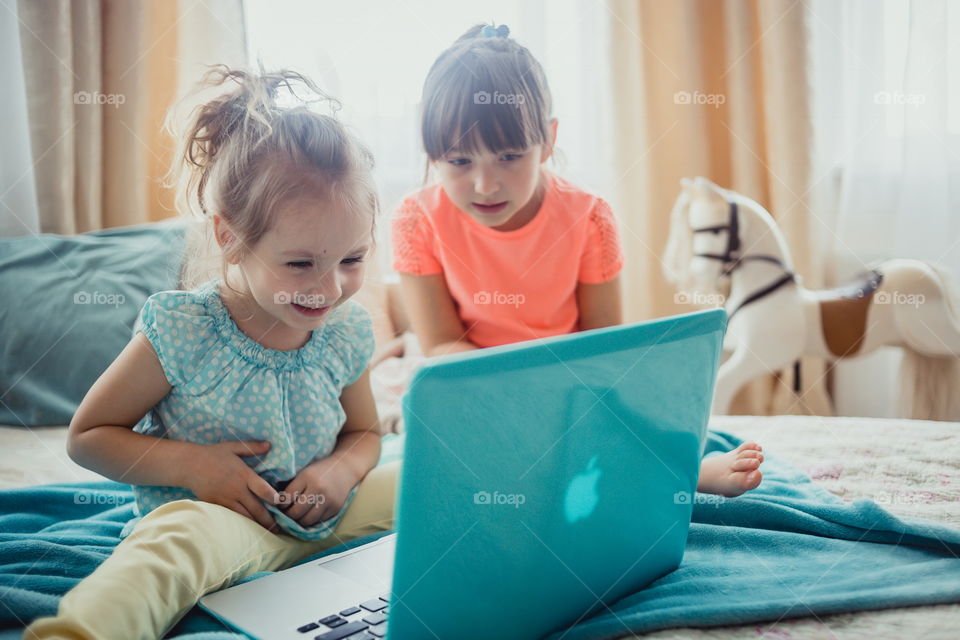 Little sisters with gadgets(laptop and tablet) in the bed.