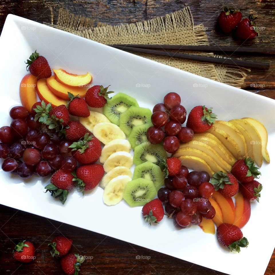 Fresh fruit on a white rectangular plate sitting on a rustic wood table. 