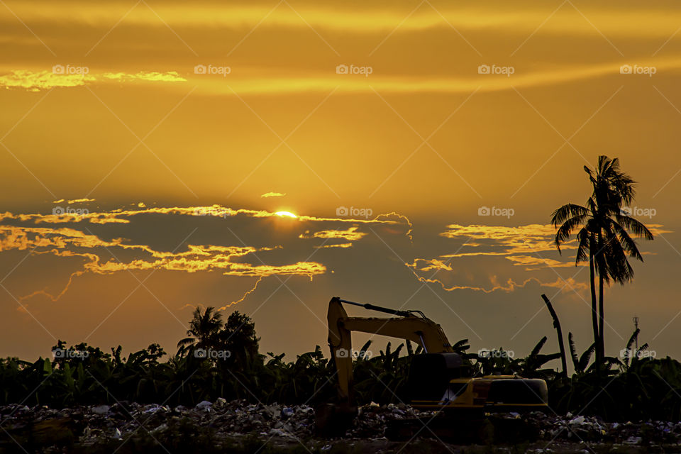 Sunset the evening light through the clouds and the shadow of Backhoe loaders On a pile of garbage.