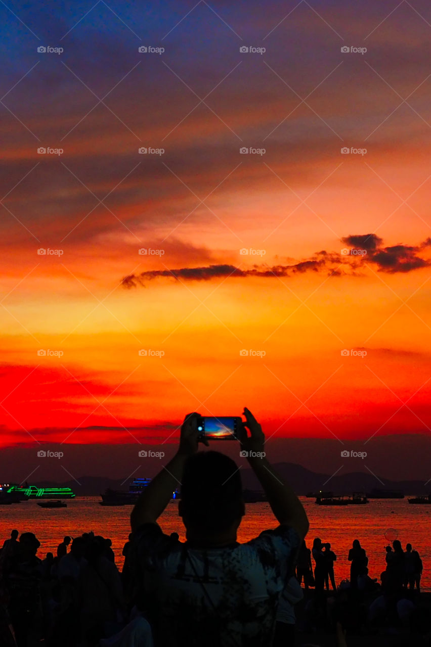 Man taking picture of beautiful landscape view and red sky during sunset.