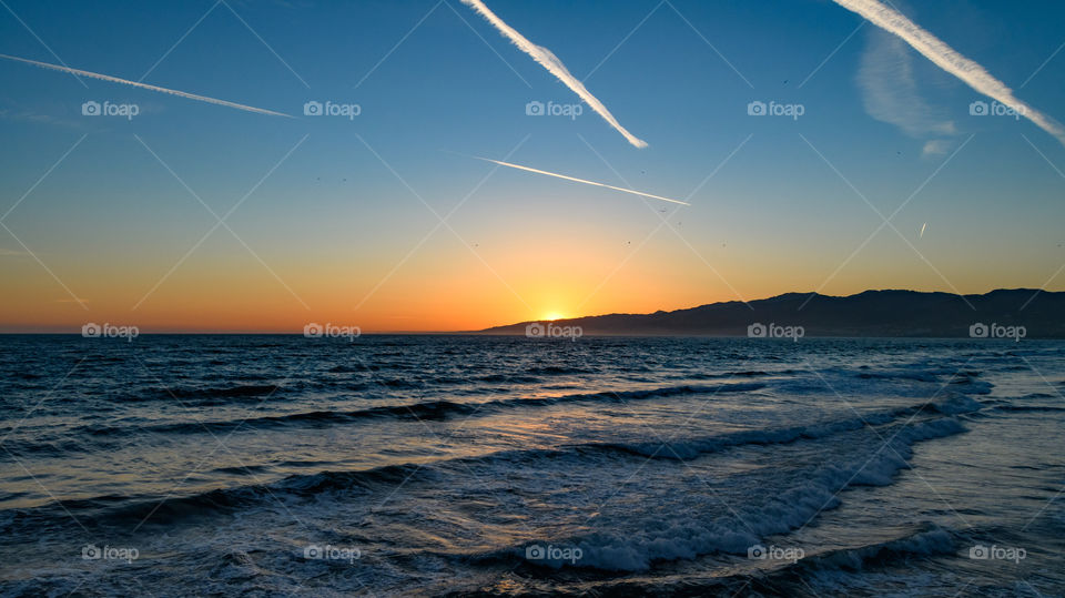 The last peek of the sun until the next day. Sunset in Santa Monica Beach, California with beautiful mountain scenery and some waves. 