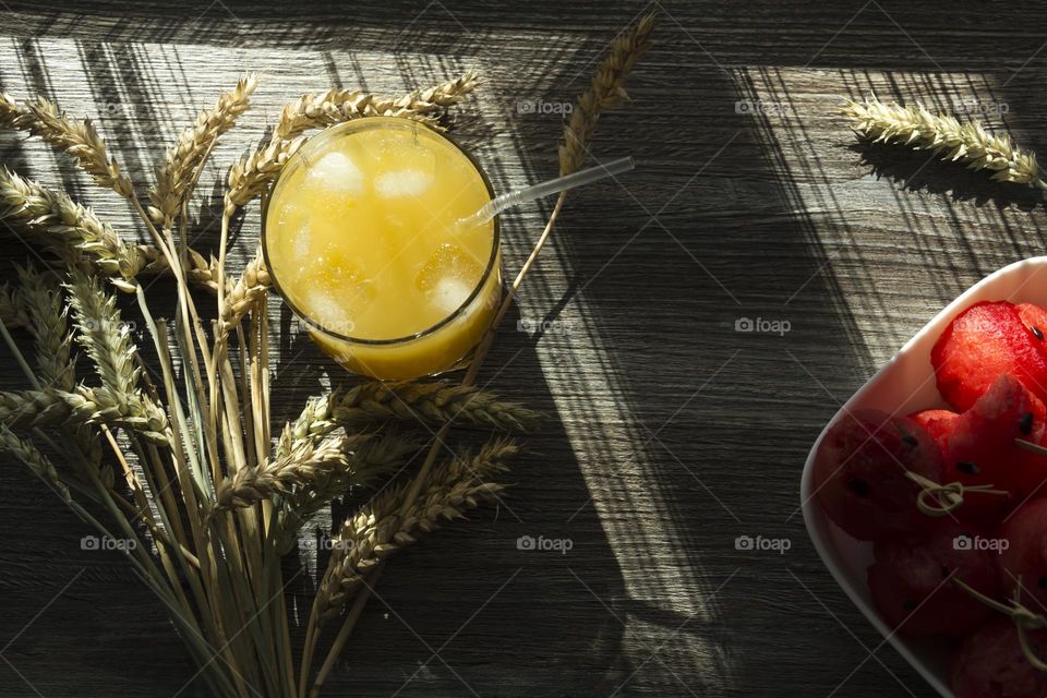 Orange juice with ice in a glass glass with spikelets of wheat on a wooden background.