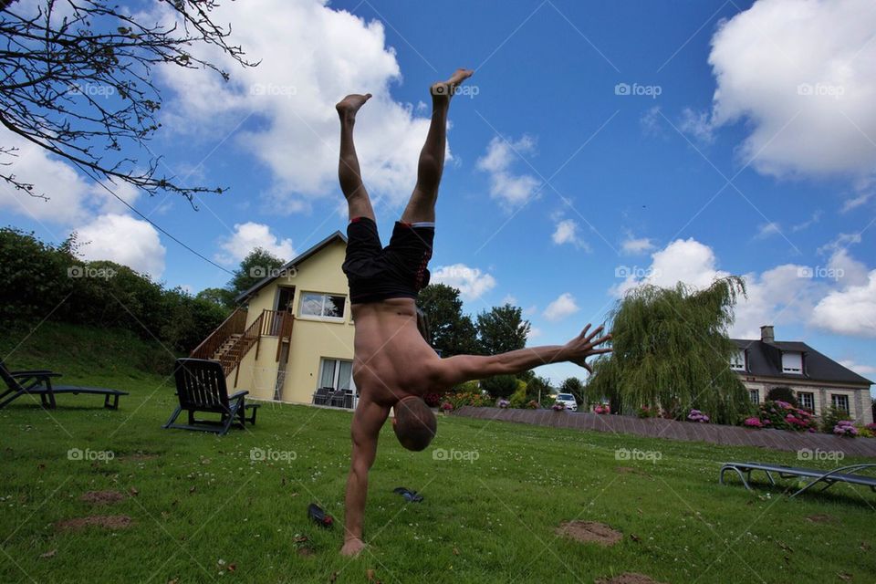 A young man doing a one hand handstand yoga pose on a green field 