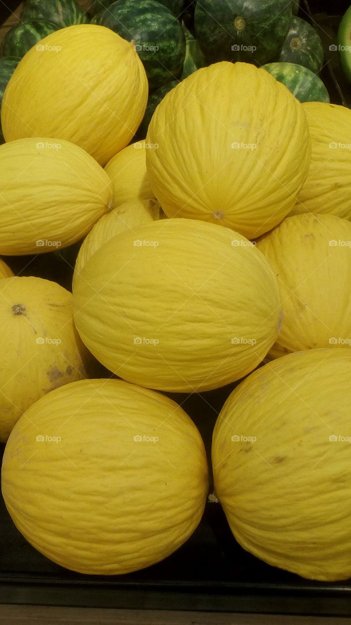 Many yelow fresh melons in market.In the backround we see group of green 
watermelons.