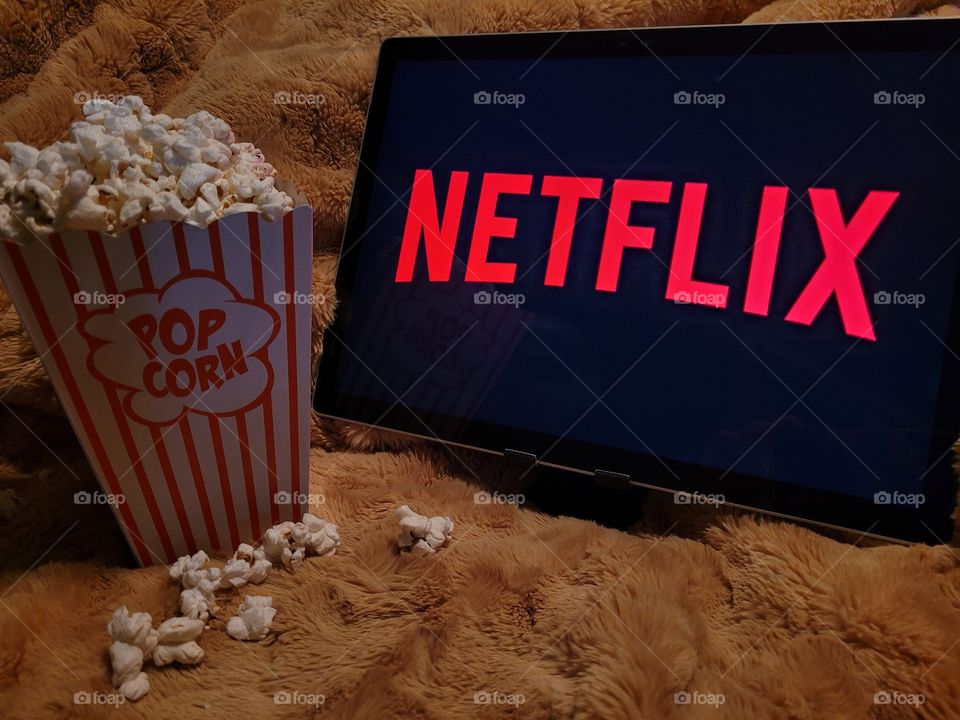 Laptop computer screen ready to watch Netflix for a fun, cozy, and relaxing night with popcorn as a snack, on soft bed blanket in dark room