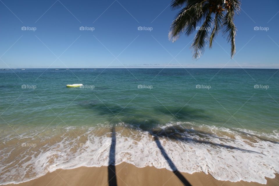 Raft, Shadows, Sea & Surf. A raft floats in mellow water while palm trees cast shadows on the beach and the sea.