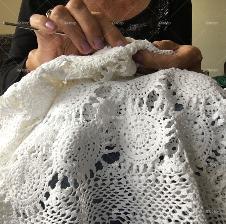 Woman crocheting fine white lace cotton tablecloth on her lap
