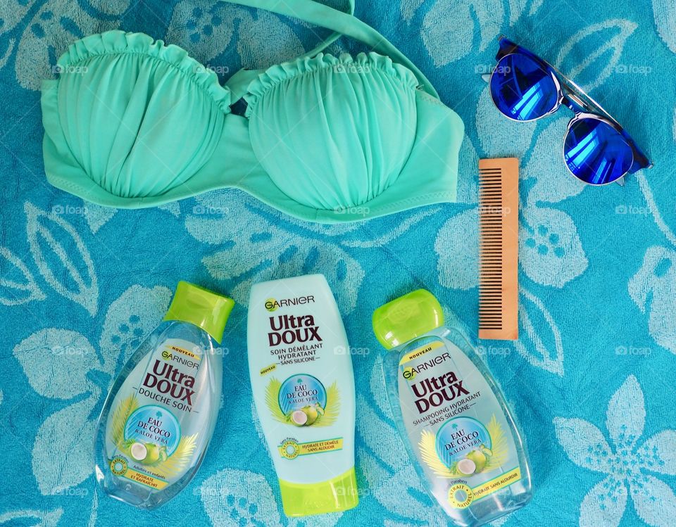 Garnier eau de coco shampooing, conditioner and bath gel on a beach towel with comb, sunglasses and a bikini top.