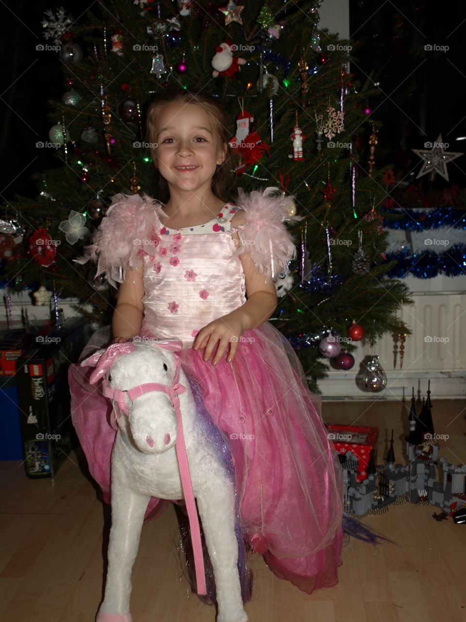 child dressed as a princess sitting on a unicorn by a large Christmas tree.
