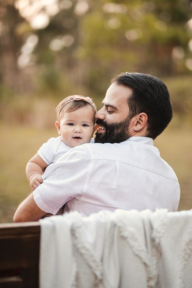 Sweet father and daughter enjoying a fun time outside at the park. Dad is holding his young baby as they sit on a bench.