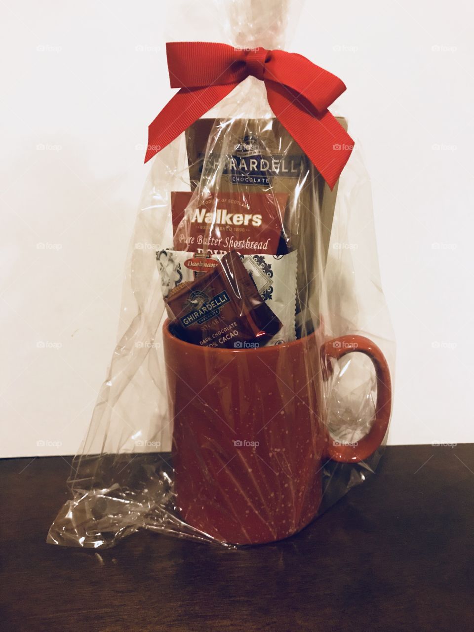 A beautiful red coffee mug filled with sweet treats if Ghirardelli chocolates and coffee tied with a little red ribbon on top for a perfect Christmas gift. USA, America