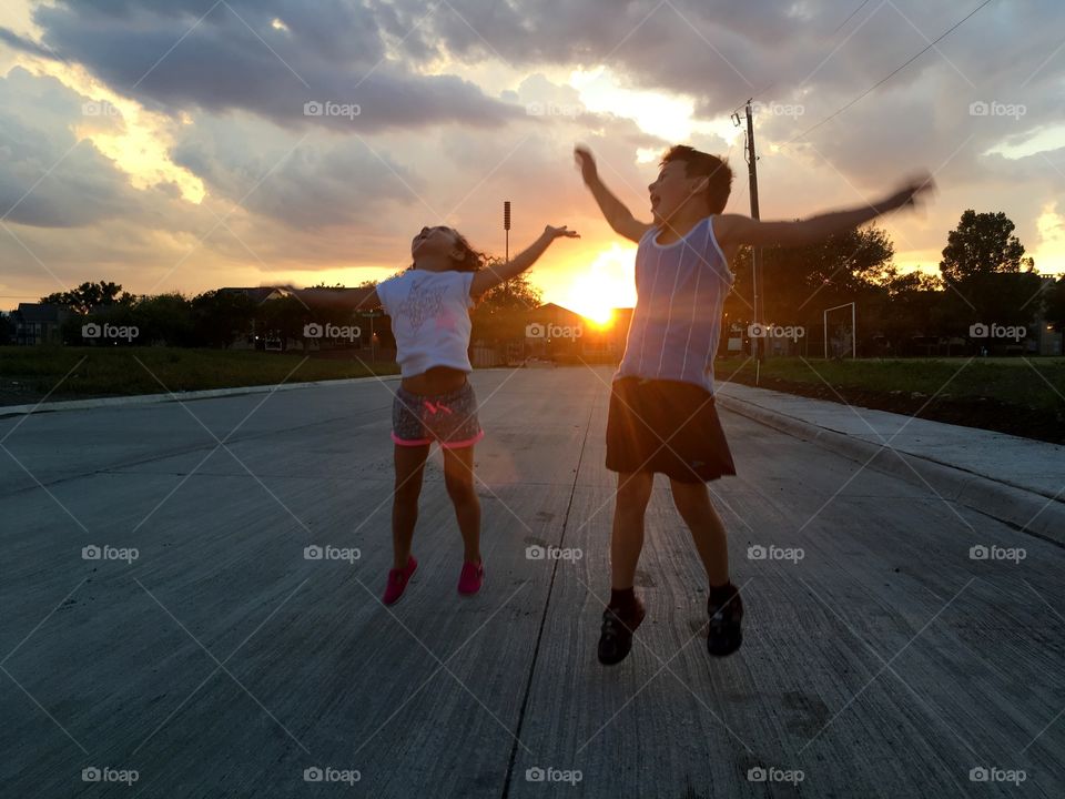 two children jumping and having fun in the street during the sunset