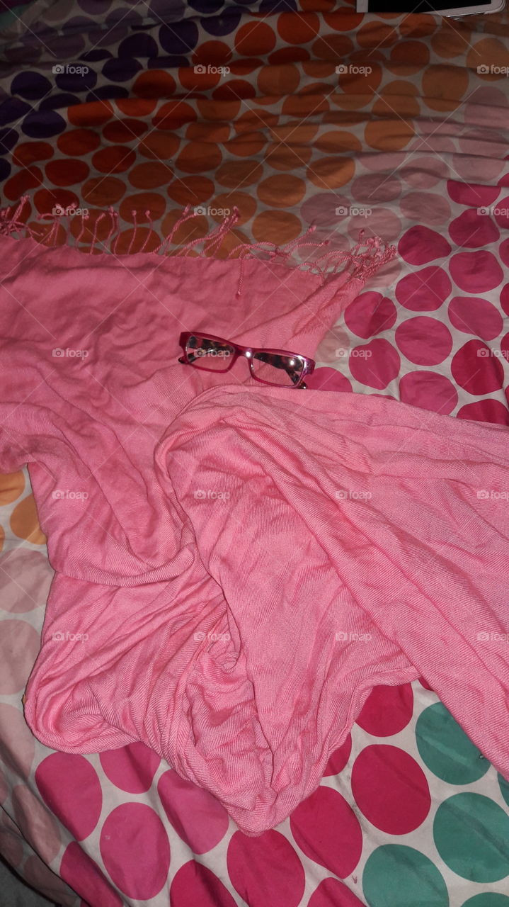 Reading glasses and a pink scarf laying on the bed.