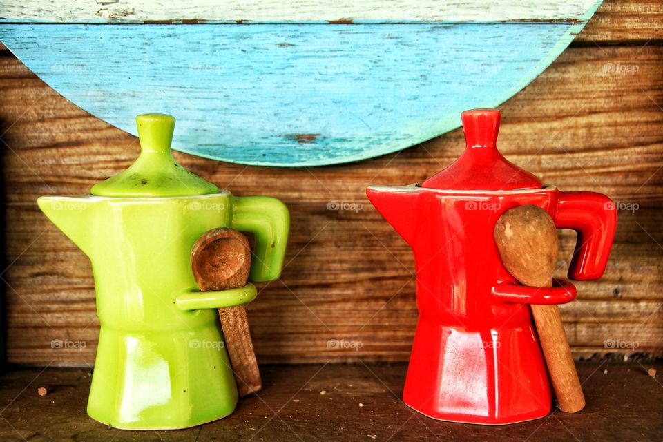 Two green and red jars with two small wooden scoops were placed side by side on the wooden floor.  Has a colorful wooden background.