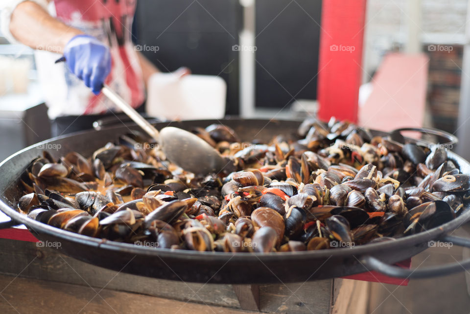 Person perparing mussels dish on huge pan