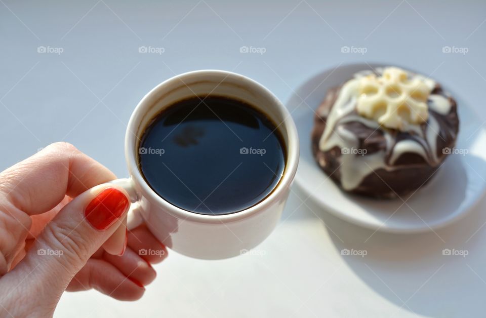 cup of coffee in the female hand and cake in sunlight on a white background