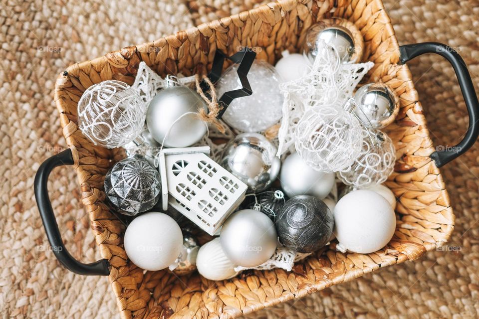 Wicker basket with white and silver Christmas tree toys and balls on floor, top view