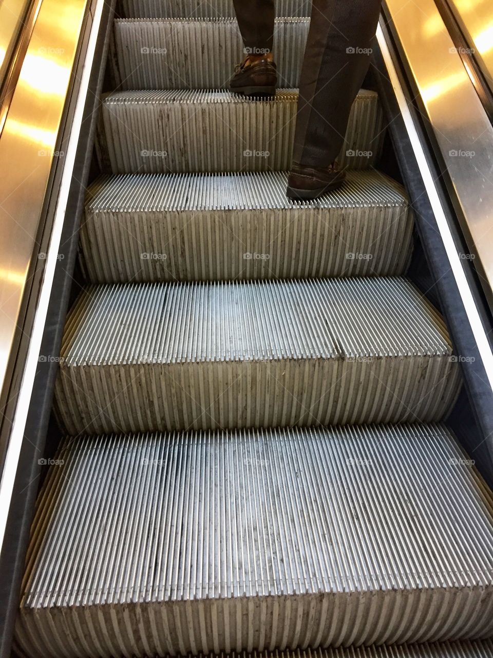 Legs of a man standing on an escalator going up